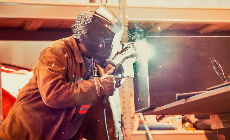 A men wearing a welding helmet and gear and working.