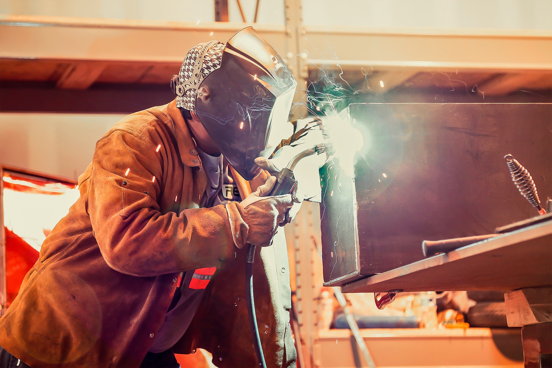 A men wearing a welding helmet and gear and working.
